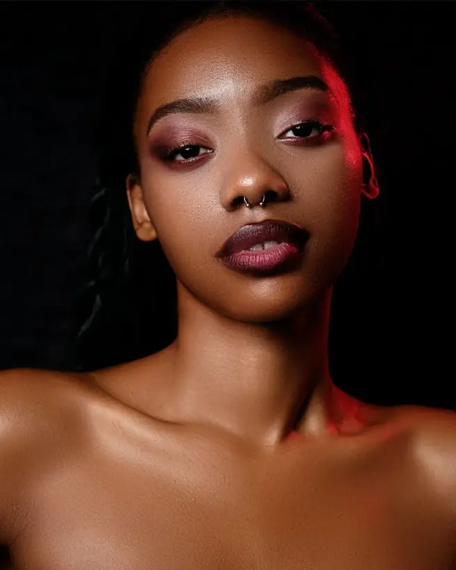 Studio beauty portrait against black, edged with a red rim light.