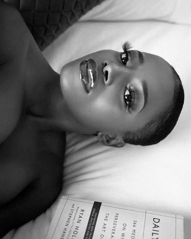 Black and white portrait lying back on a pillow beside scattered newspapers.